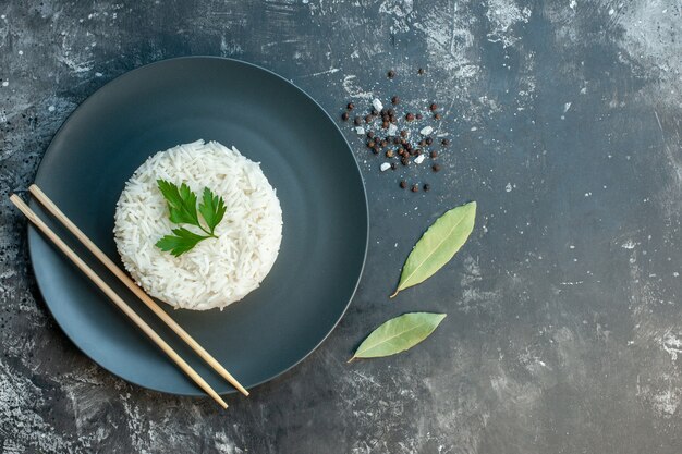 어두운 배경의 오른쪽에 있는 검은 접시 고추에 녹색과 젓가락으로 제공되는 맛있는 쌀 식사의 상위 뷰