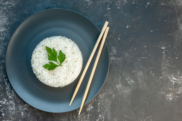 Top view of delicious rice meal served with green and chopsticks on a black plate on the right side on dark background