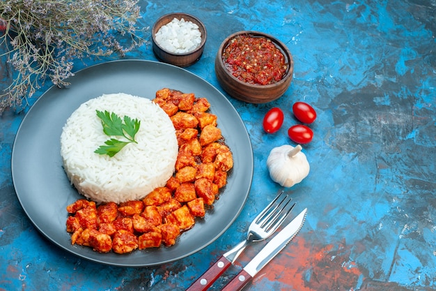 Top view of delicious rice meal with green and tomato chicken cutlery set salt garlic tomatoes on the right side on blue background