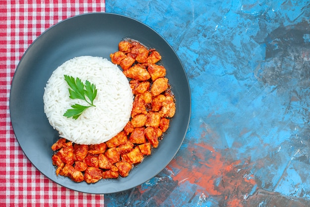 파란색 테이블에 빨간색 벗겨진 수건에 녹색 및 토마토 치킨을 곁들인 맛있는 쌀 식사의 상위 뷰