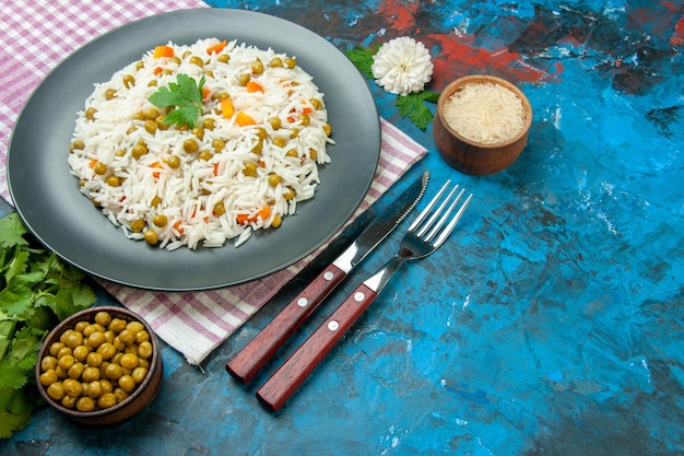 Vista dall'alto di una deliziosa farina di riso con fagotto verde carota pisum su asciugamano viola e posate su sfondo blu Foto Gratuite