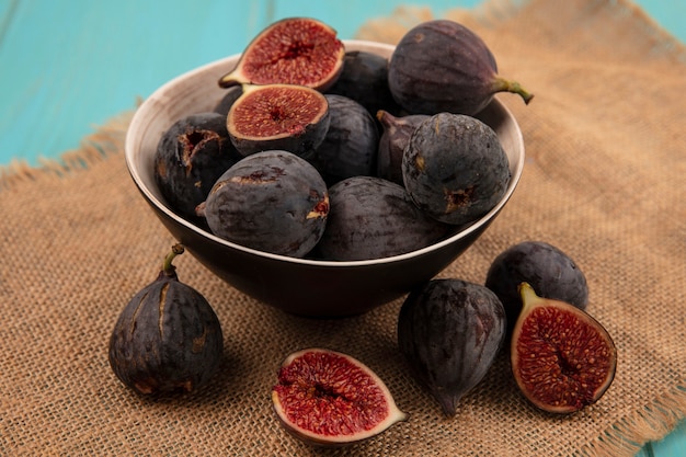 Free photo top view of delicious ripe black mission figs on a bowl on a sack cloth on a blue wall