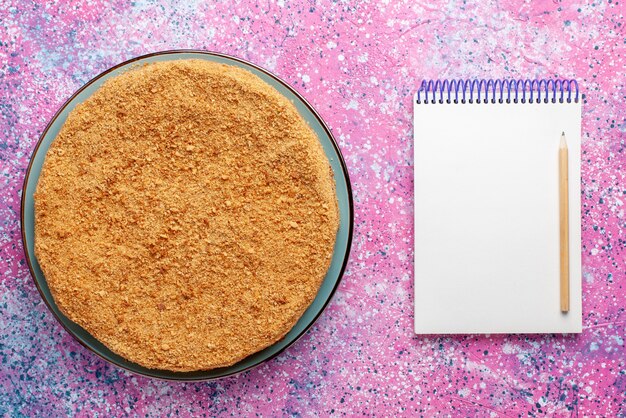 明るい机の上のメモ帳とガラス板の中のおいしい丸いケーキの上面図ケーキパイビスケット甘い焼き砂糖