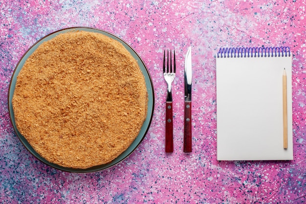 Вид сверху вкусный круглый торт внутри тарелки со столовыми приборами и блокнотом на ярком столе торт пирог бисквит сладкая выпечка сахар