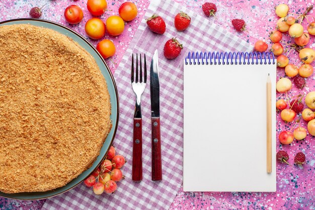 Top view delicious round cake inside plate with fruits and notepad on bright pink desk cake pie biscuit sweet bake sugar