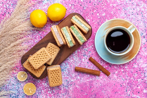 Top view delicious sandwich cookies with lemon tea and cinnamon on pink desk.