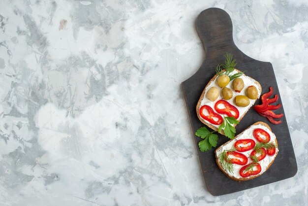Foto gratuita vista dall'alto deliziosi panini con peperoni e olive sul tagliere sfondo bianco pranzo cibo pane cena spuntino panino pasto orizzontale