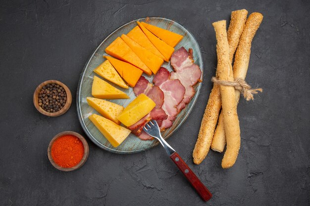 Вид сверху вкусной колбасы и ломтика сыра на синей тарелке с перцем на темном фоне