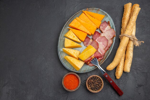 Вид сверху вкусной колбасы и ломтика сыра на синей тарелке с перцами слева на темном фоне