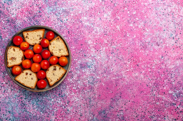 Вид сверху вкусного нарезанного торта с кислыми свежими сливами внутри сковороды на светло-розовой поверхности