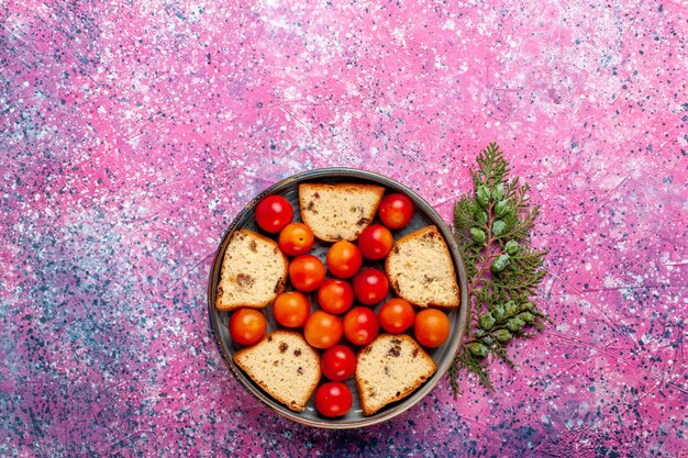 Вид сверху вкусного нарезанного торта с кислыми свежими сливами внутри сковороды на розовой поверхности