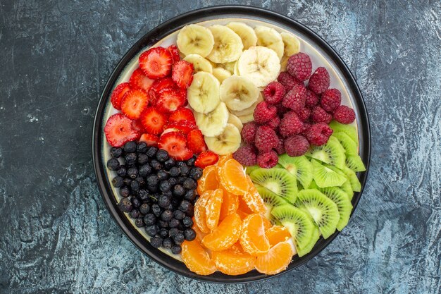 Вид сверху вкусных нарезанных фруктов внутри тарелки на сером экзотическом цвете, фото здорового образа жизни, спелое дерево