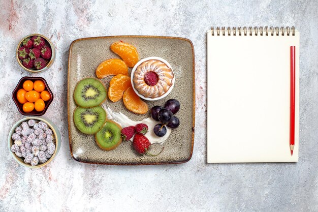 Top view delicious sliced fruits with cake and candies on a white background fruit fresh tea candy cake biscuit