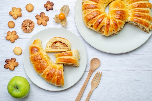 Top view of delicious sliced pastries inside plate with filling along with wooden fork spoon cookies on white desk, pastry cookie biscuit sweet sugar