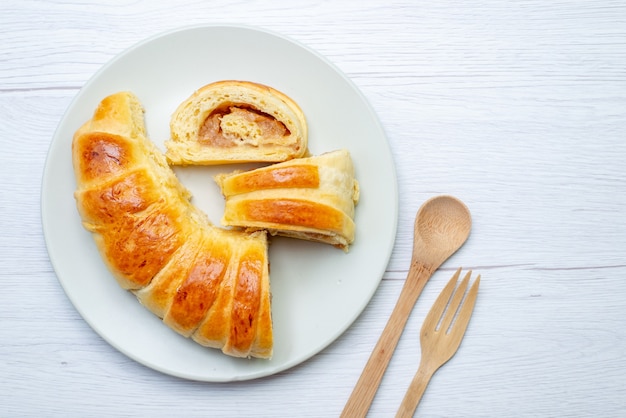 Top view of delicious sliced pastries inside plate with filling along with wooden fork spoon on white desk, pastry cookie biscuit sweet