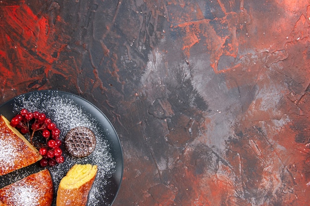 Вид сверху вкусный нарезанный пирог с красными ягодами на темном полу сладкий пирог