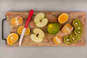 Foto gratuita vista dall'alto di delizioso mandarino a fette con fette di kiwi e mela su una tavola di cucina in legno con coltello