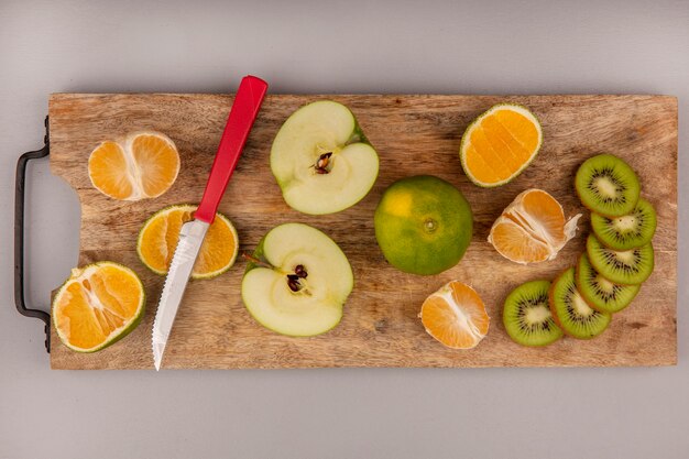 Top view of delicious sliced tangerine with kiwi and apple slices on a wooden kitchen board with knife