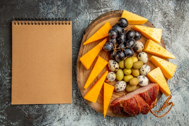 Top view of delicious snack including fruits and foods for wine on a brown tray and notebook on gray table