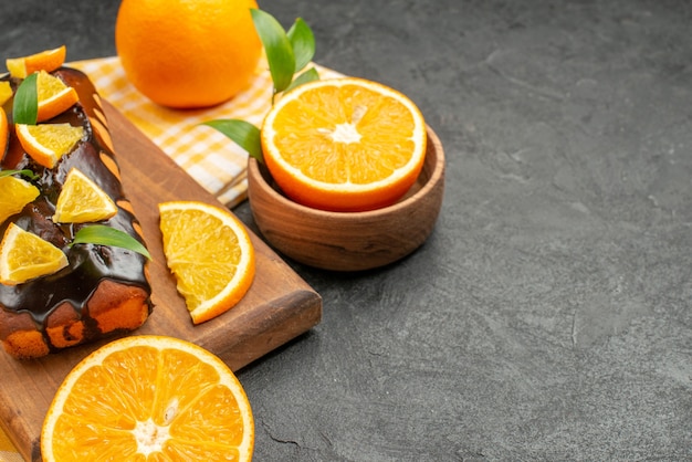 Top view of delicious soft cakes whole and cut lemons with leaves on dark table