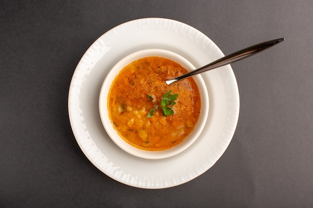 Вид сверху вкусного супа внутри тарелки с ложкой на темной поверхности