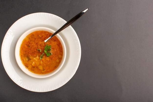 Top view of delicious soup inside plate with spoon on dark surface