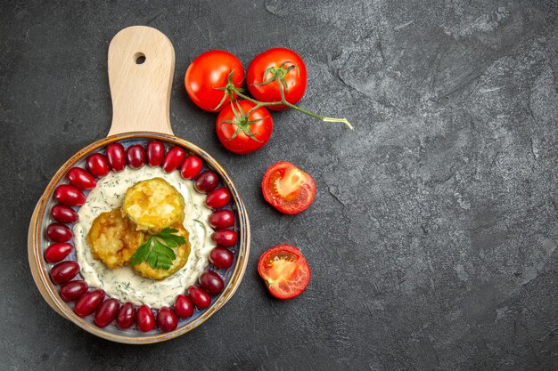 Top view of delicious squash meal with fresh red dogwoods and tomatoes on grey surface