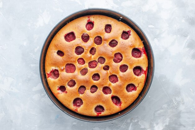 真っ白な机の上の鍋で新鮮な赤いイチゴで焼いたおいしいストロベリーケーキの上面図、ケーキビスケットフルーツ甘い生地焼き