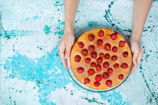 青い机の上と内側に果物、ケーキ生地の甘いビスケットで丸い形のおいしいストロベリーケーキの上面図