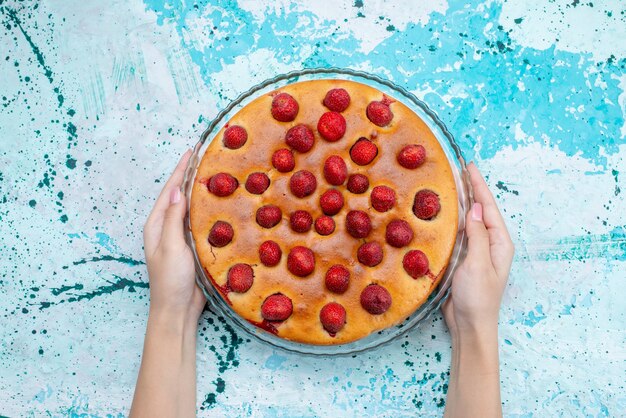 明るい青色の机の上と内側に果物が丸い形をしたおいしいストロベリーケーキの上面図、ケーキ生地の甘いビスケット