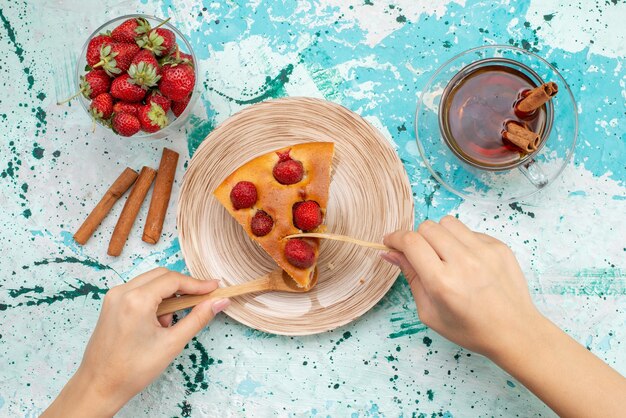 Top view of delicious strawberry cake sliced yummy cake getting eat with tea cinnamon and fresh red strawberries on bright-blue desk, cake bake dough sweet