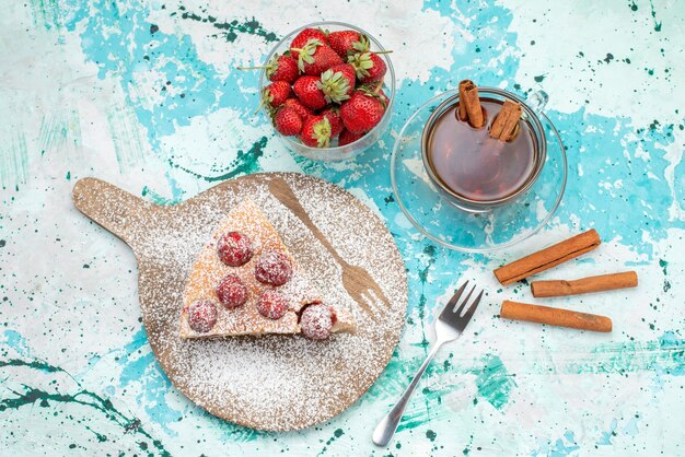 Top view of delicious strawberry cake sliced yummy cake sugar powdered with tea on bright-blue, berry cake sweet bake dough