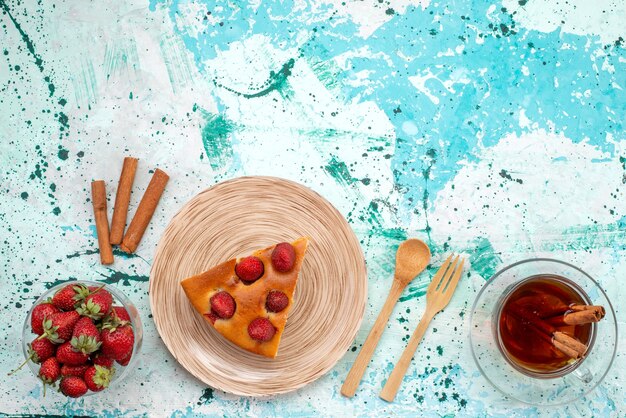 Top view of delicious strawberry cake sliced yummy cake with tea cinnamon and fresh red strawberries on bright-blue desk, berry cake bake dough