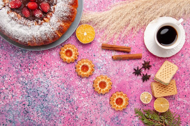 Top view delicious strawberry cake sugar powdered cake with waffles cookies and cup of tea on light pink desk cake sweet sugar cookies pie