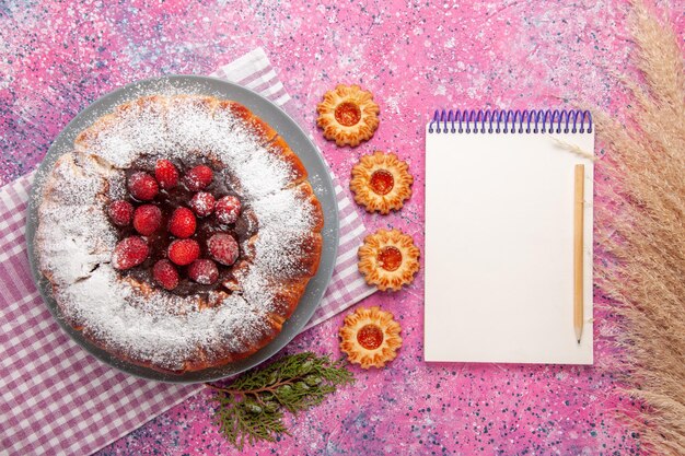 Top view delicious strawberry cake with notepad and  on light pink surface