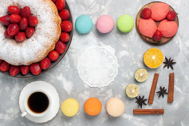 Foto gratuita vista dall'alto deliziosa torta di fragole con macarons e tazza di tè su bianco chiaro