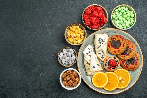 Top view delicious sugar cookies with pastries candies and orange slices on dark surface sugar biscuit sweet cake cookie tea