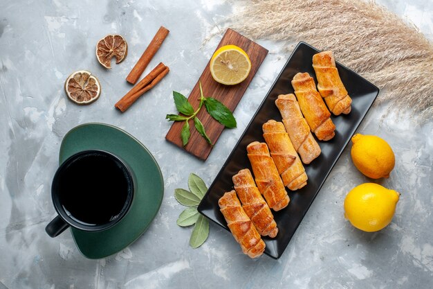 Top view delicious sweet bangles with lemon cinnamon and tea on light table, pastry cake bake sweet sugar