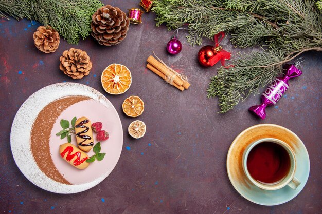 トップビュー暗い背景の上のお茶とクリスマスツリーとおいしい甘いビスケットクッキー甘いビスケット砂糖色のケーキ