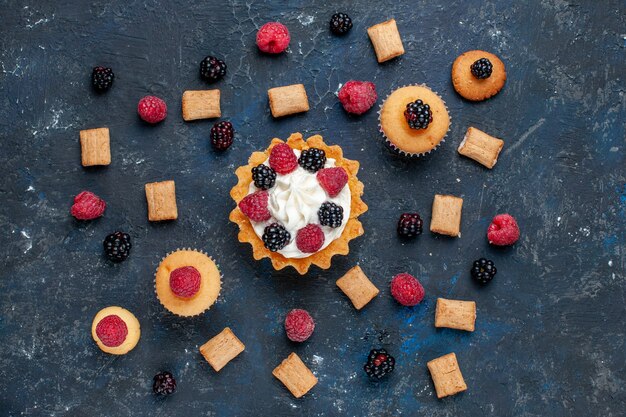 Top view of delicious sweet cake with different berries cookies and yummy cream on dark-grey, fruit berry color cake biscuit sweet bake