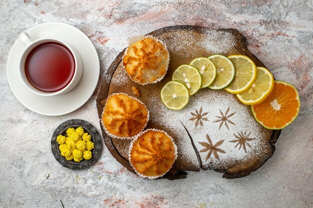 Вид сверху вкусные сладкие пирожные с дольками лимона и чашкой чая на белой поверхности