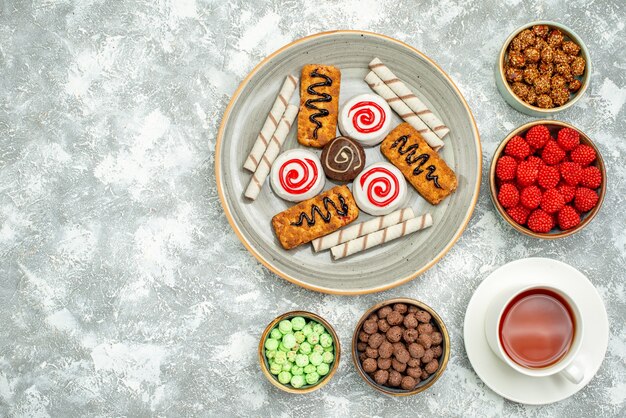 Top view delicious sweet candies with cookies and cup of tea on white space