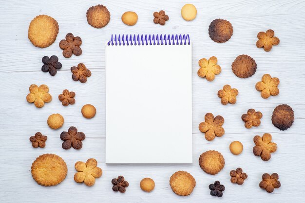 ライトデスクのメモ帳、クッキービスケットの甘い砂糖と一緒に形成されたさまざまなおいしい甘いクッキーの上面図