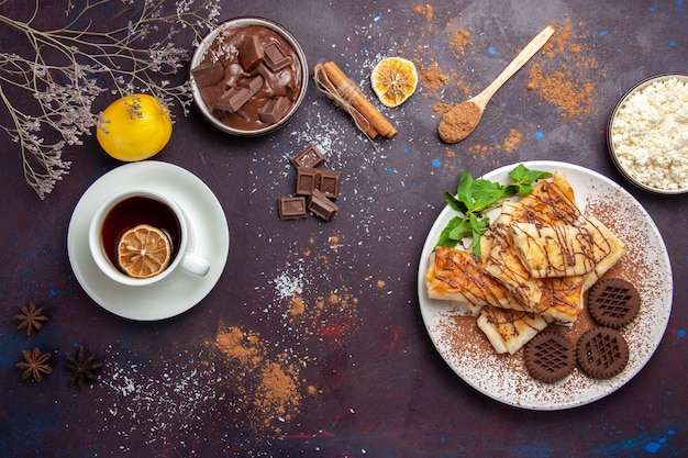 Vista dall'alto deliziosi pasticcini dolci con biscotti al cioccolato e tazza di tè in uno spazio buio