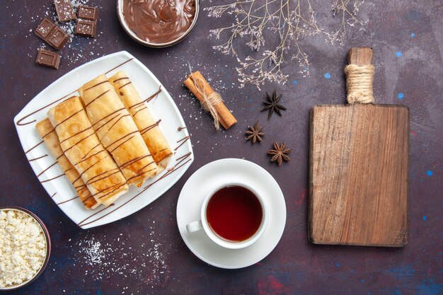 Top view delicious sweet pastries with chocolate and cup of tea on dark floor sweet bake biscuit dessert sugar cake