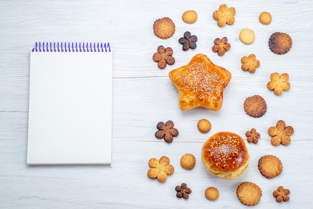 Top view of delicious sweet pastries with cookies and notepad on light desk, pastry cookie biscuit sweet sugar