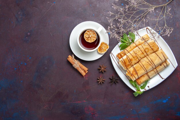 Top view delicious sweet pastries with cup of tea on dark space