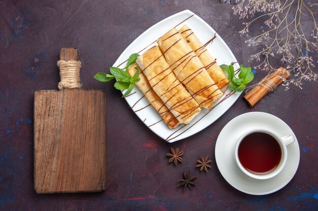 Top view delicious sweet pastries with cup of tea on dark space