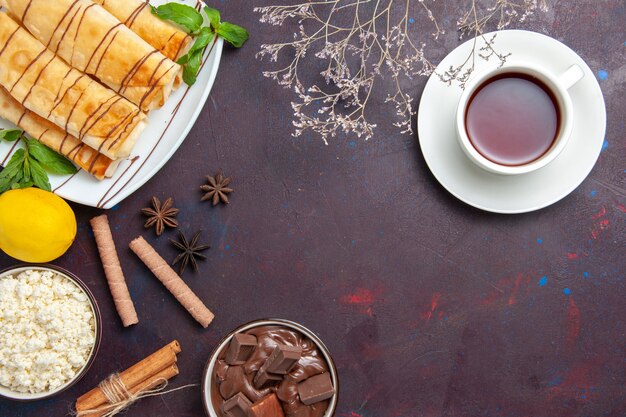 Top view delicious sweet pastries with lemon and cup of tea on dark space