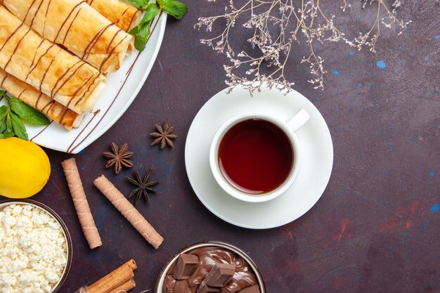 Top view delicious sweet pastries with lemon and cup of tea on dark space